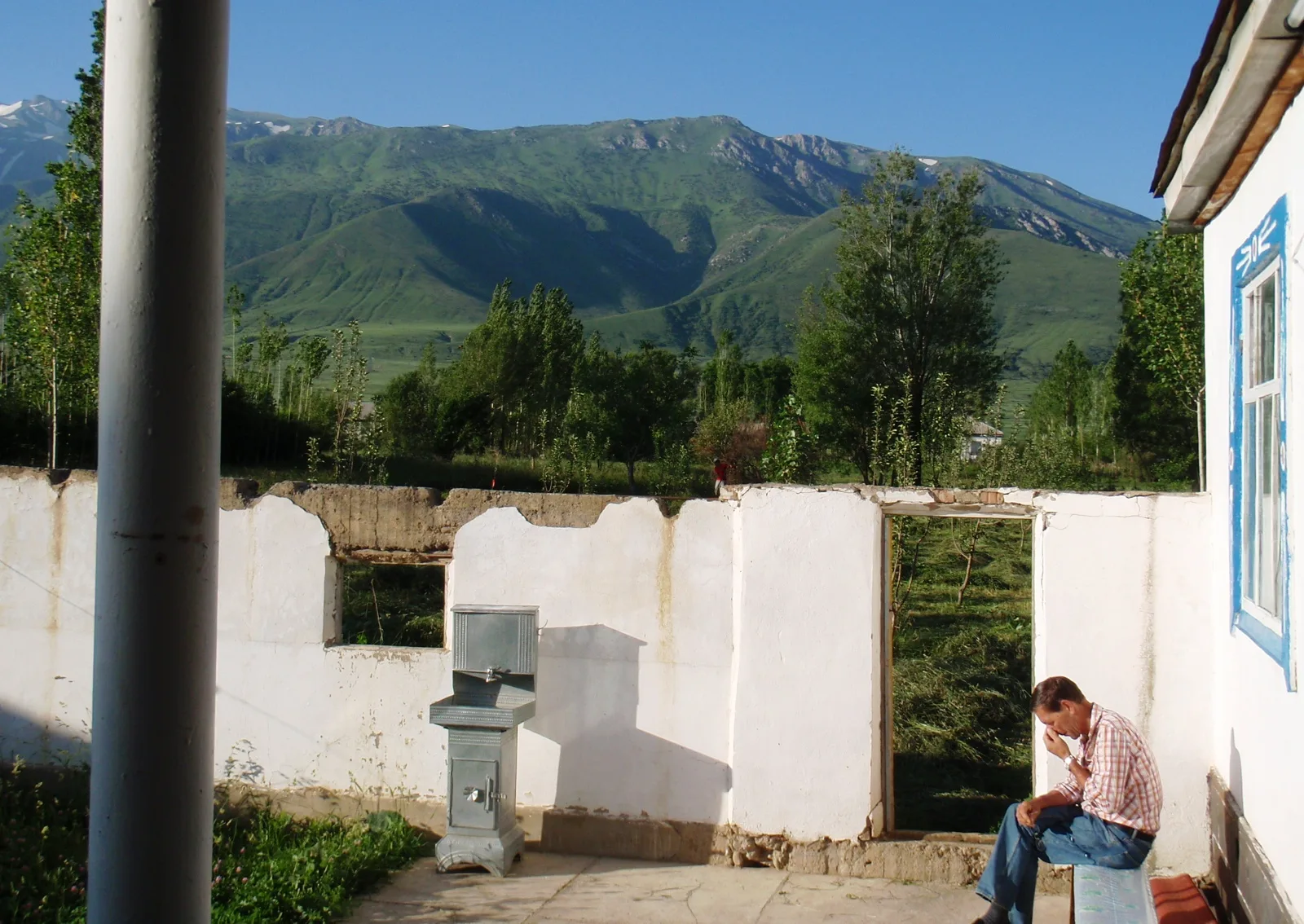 A modest single-storey guesthouse in a Kazakhstan national park village, with a whitewashed facade and a small garden, typical of rural homestay accommodation in the Zhetysu steppe.