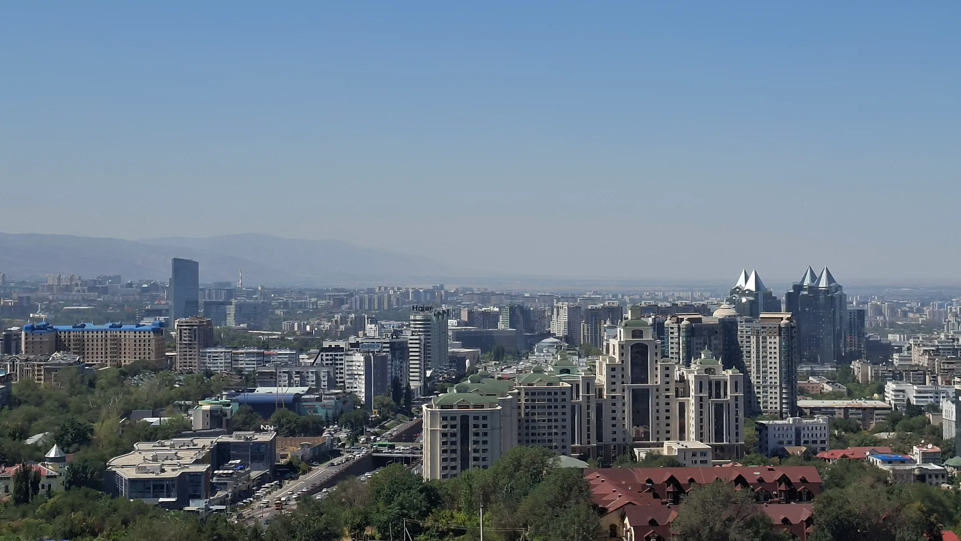 Almaty city skyline panorama viewed from Kök Töbe hill, showing the urban cityscape with mountains in the background.
