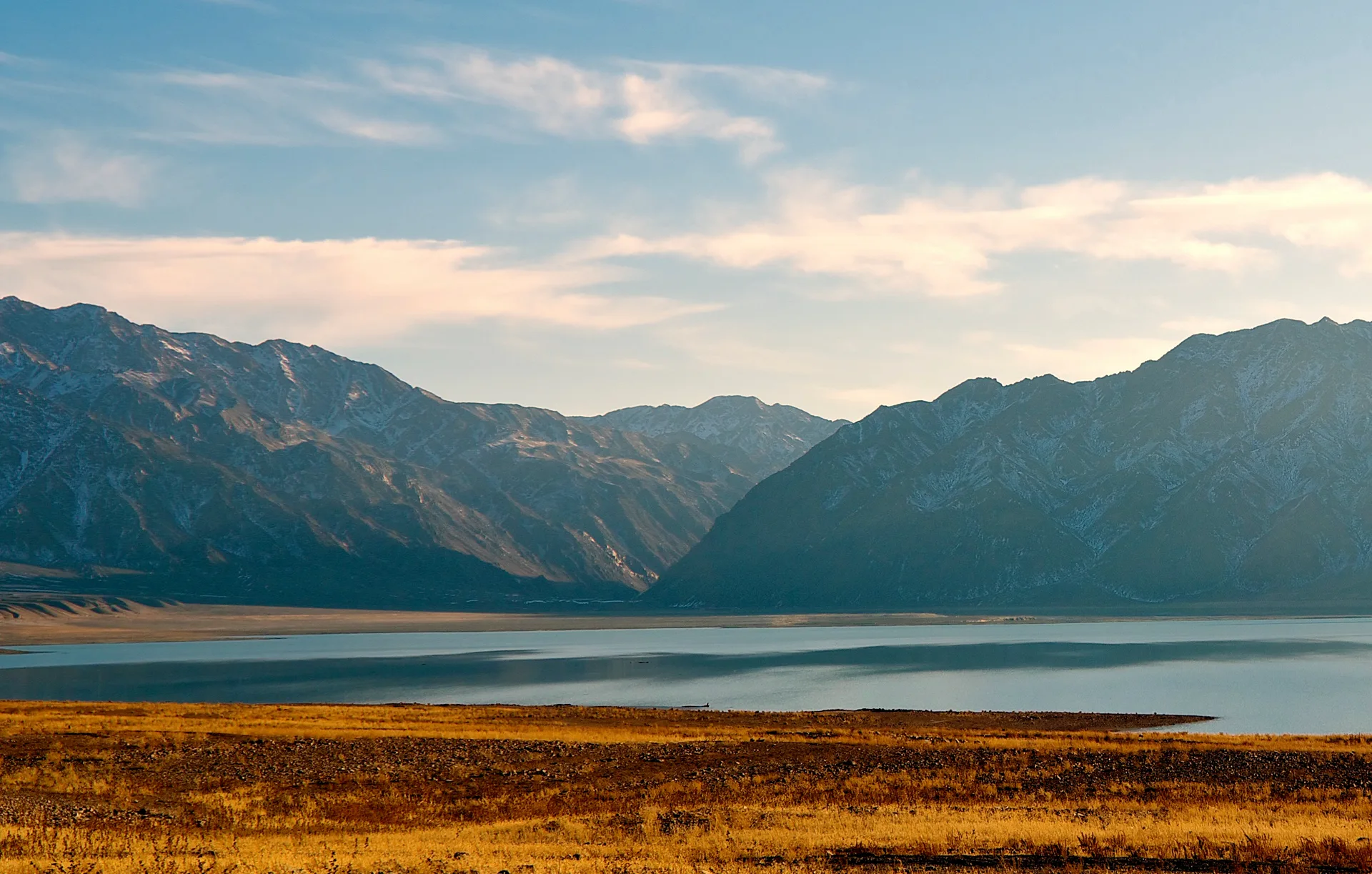 Bartogay Reservoir in autumn, the turquoise water enclosed by golden-brown slopes of the Chilik valley under an overcast sky.