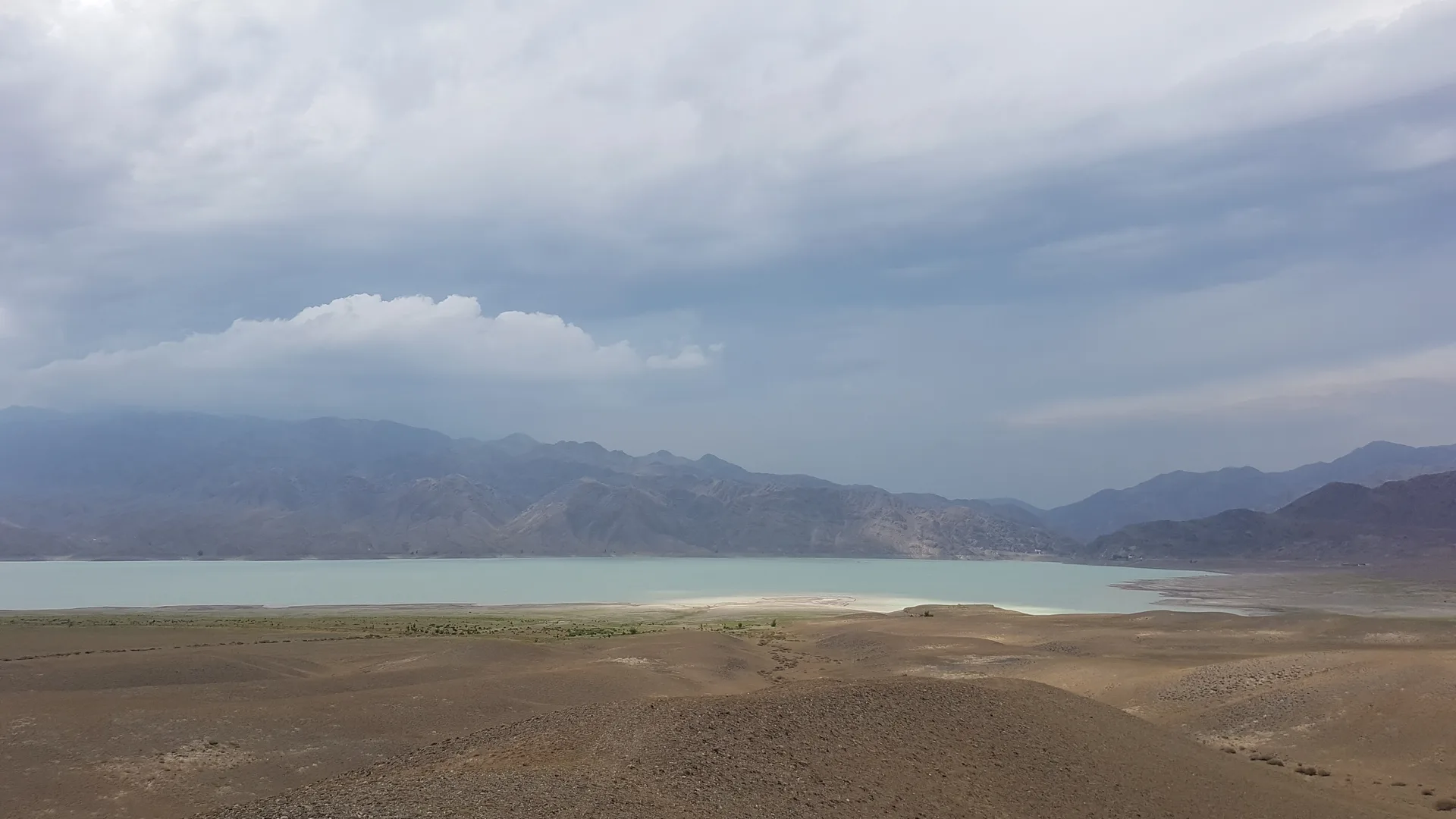 Bartogay Reservoir on the Chilik River with the Tien Shan mountain backdrop under clear blue sky.