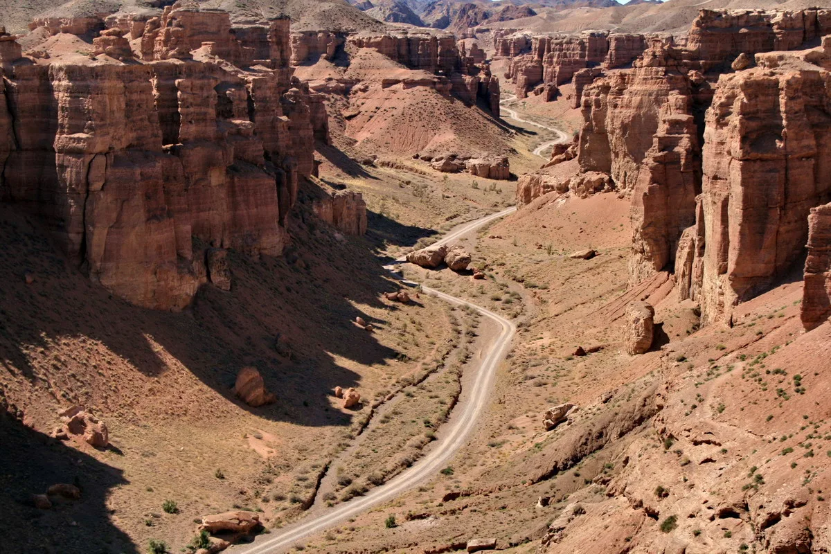Aerial view of Charyn Canyon's Valley of Castles, with towering red-orange sandstone columns rising on both sides of a winding road on the canyon floor.