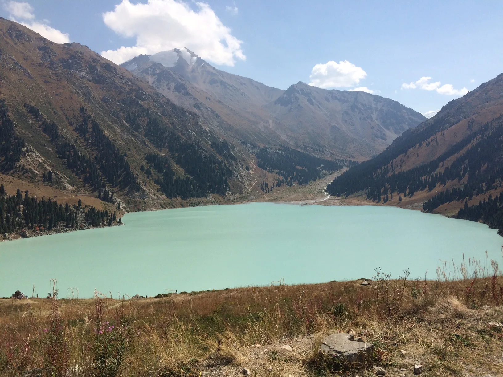 Big Almaty Lake at 2,511 m with the snow-covered summit of Peak Sovetov at 4,317 m rising beyond the turquoise water in early September.