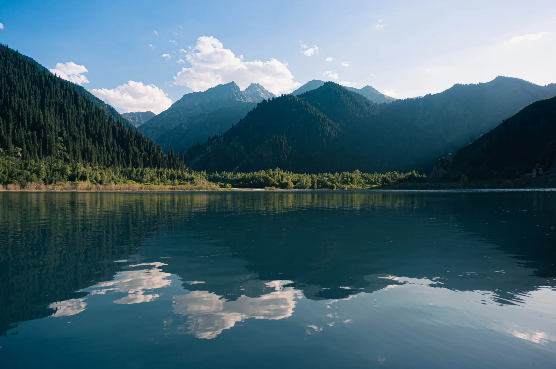 Turquoise water of Issyk Lake reflecting forested mountain slopes on a clear summer day.