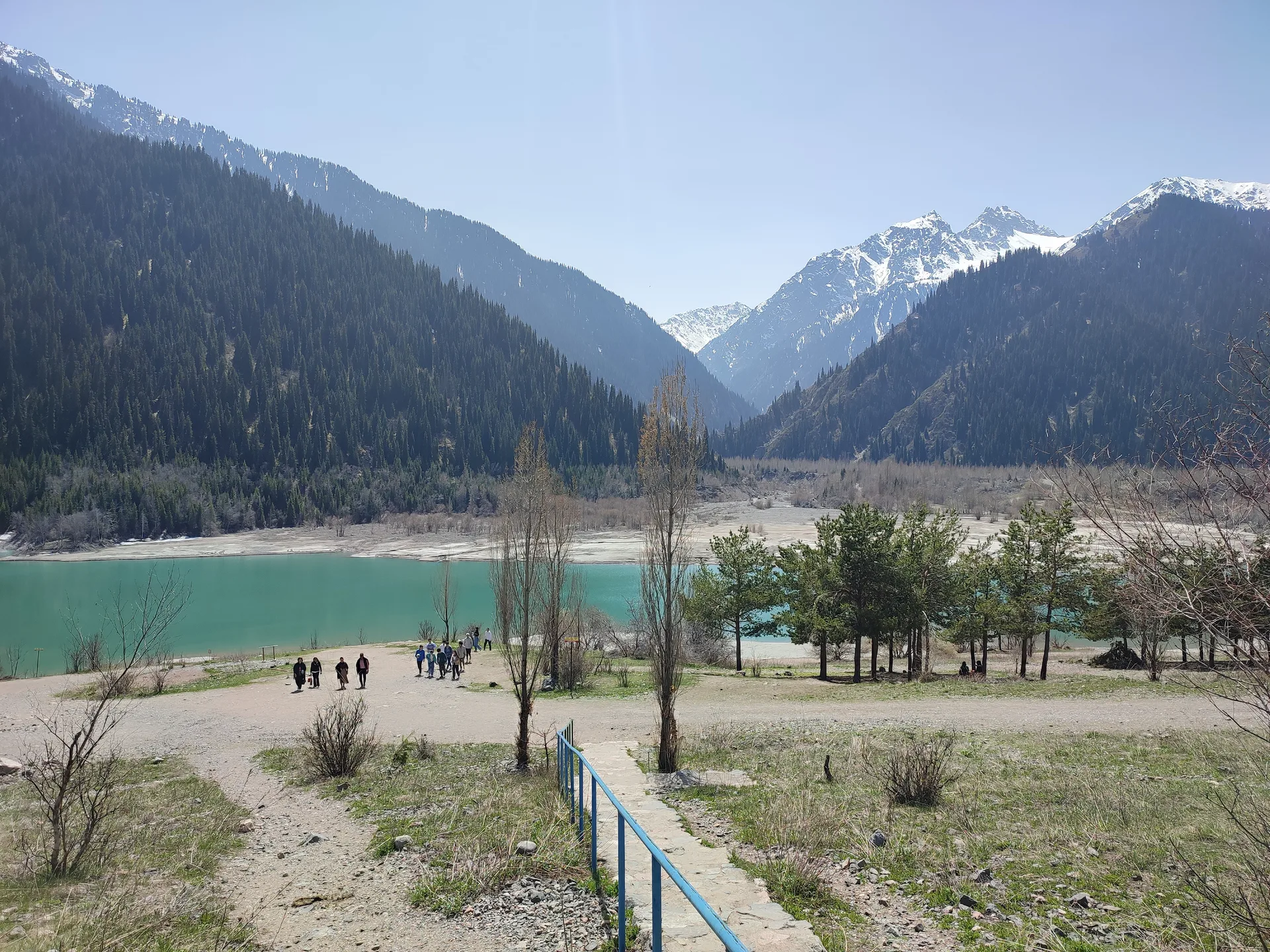 Turquoise water of Issyk Lake in the Ile-Alatau National Park gorge, with snow-capped peaks and spruce forest in spring.