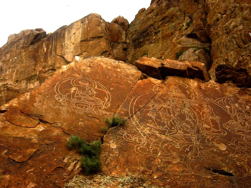 Buddhist stone carvings of seated Buddha figures carved into a sandstone cliff above the Ili River at Tamgaly-Tas, Kazakhstan.