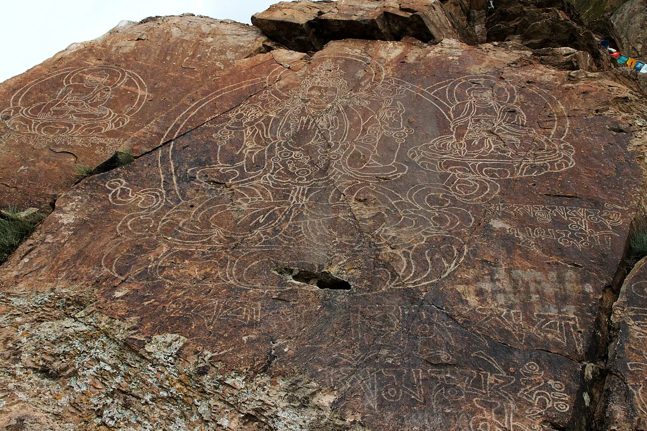 Detailed sandstone rock face at Tamgaly-Tas showing carved Buddhist figures and Tibetan script on cliffs above the Ili River.