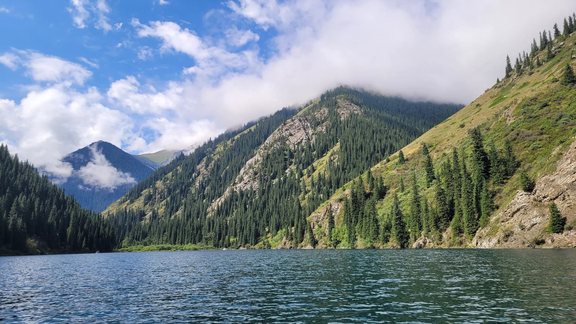 View of the lower Kolsai Lake with deep green spruce forest rising from the water's edge.