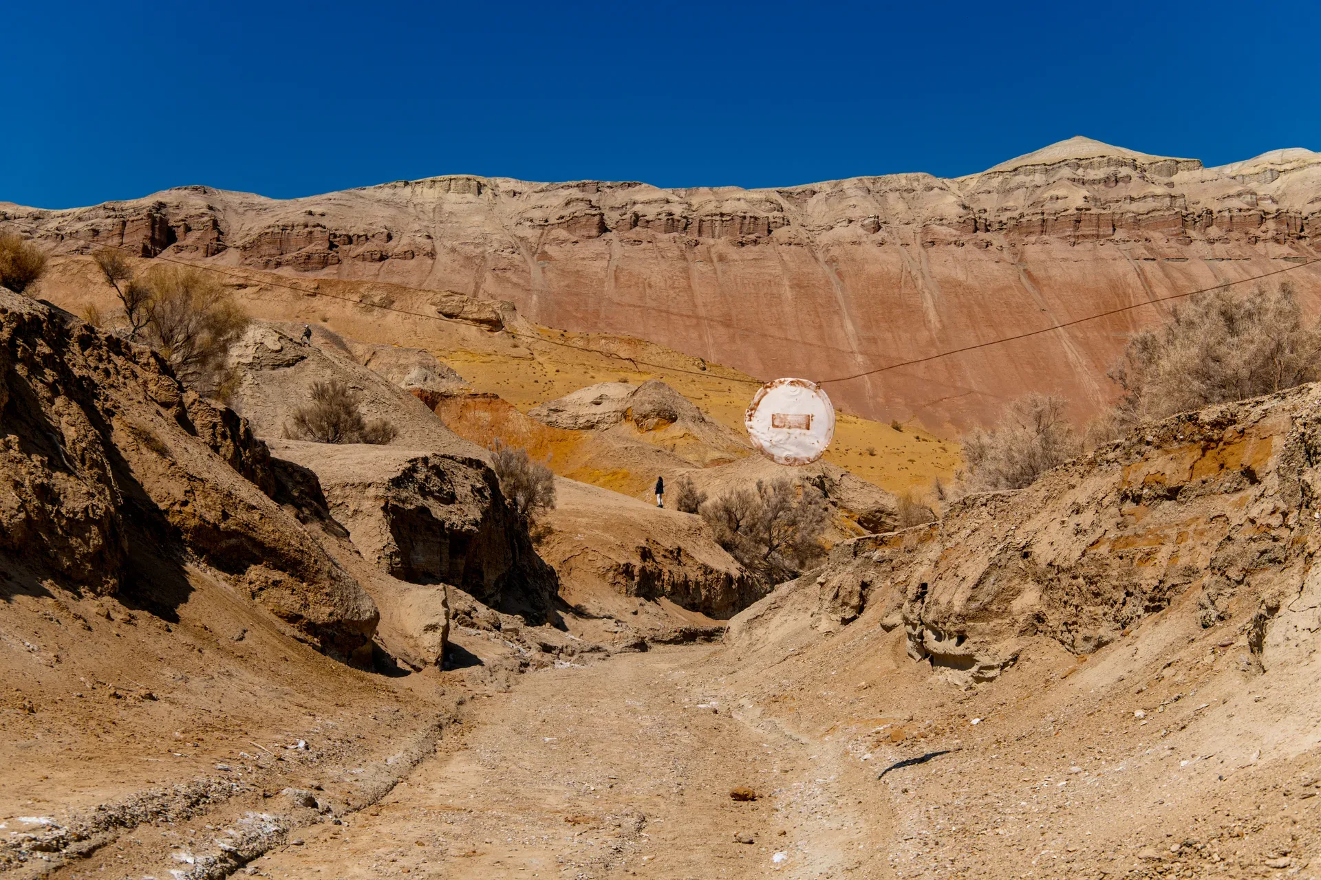 Interior of an Aktau mountain gorge showing close-up layered geological strata in ochre, white, and rust-red, with deeply eroded clay channels on either side