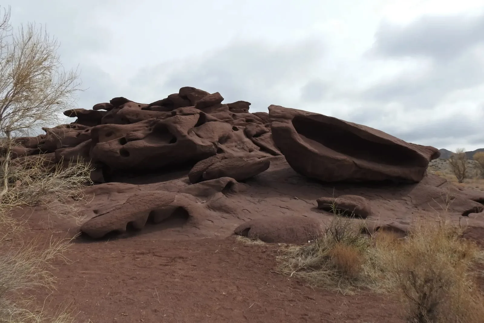 Context near Basshi Village: Dark reddish-brown volcanic rock formations of Katutau rising above desert scrub under overcast sky.