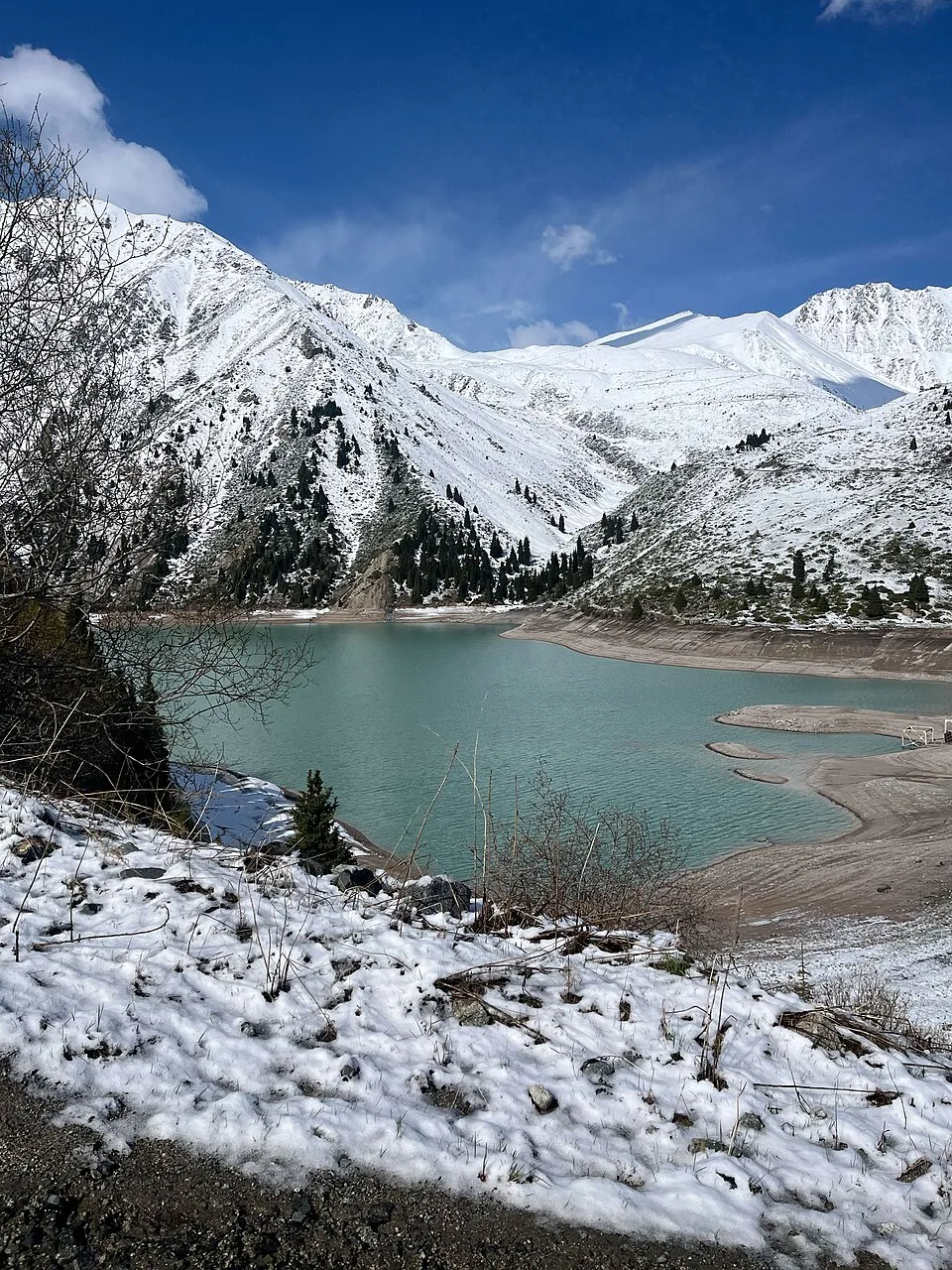 Snow-covered winter basin around Big Almaty Lake with frozen slopes and pale sky.