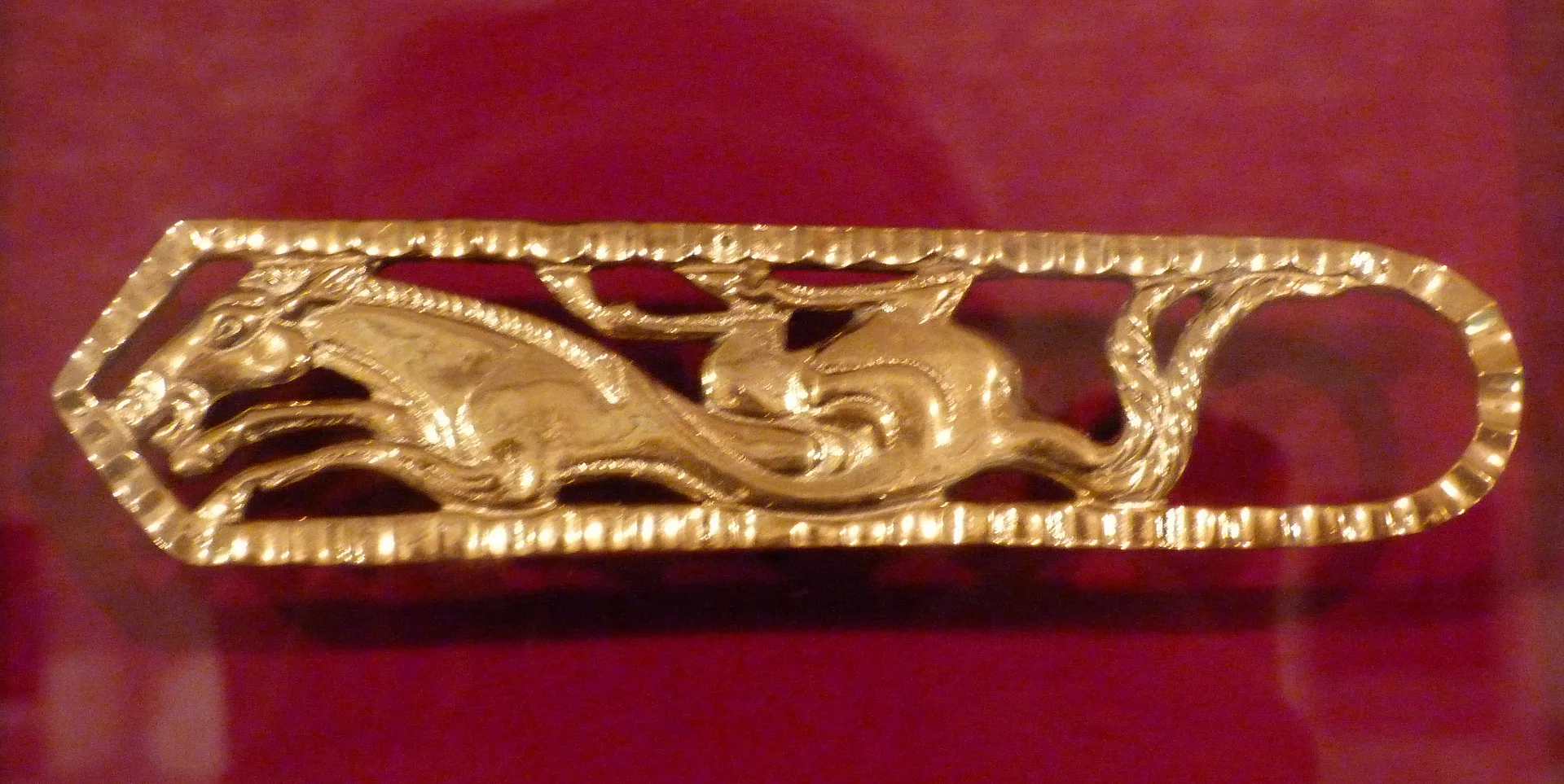 Gold horse plaque from the Issyk burial mound displayed against a dark museum background.