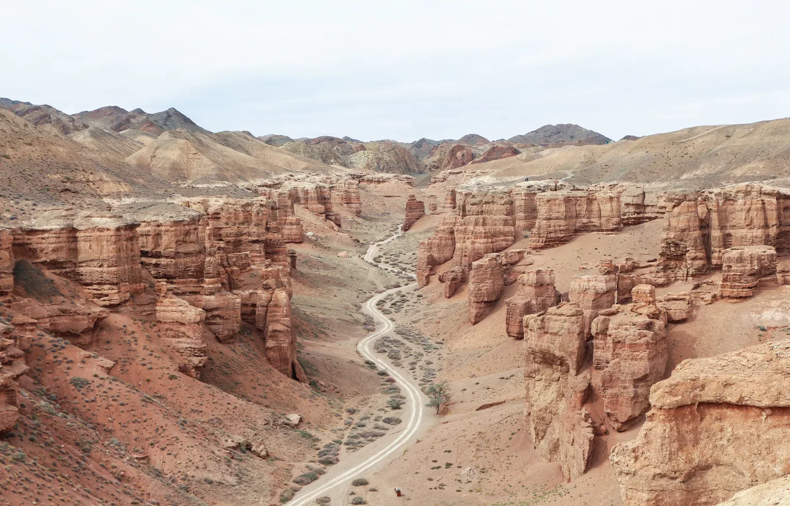 Context near Charyn Canyon Optional Loop: Dirt road winding below rust-red towers in Charyn Canyon viewed from the rim.