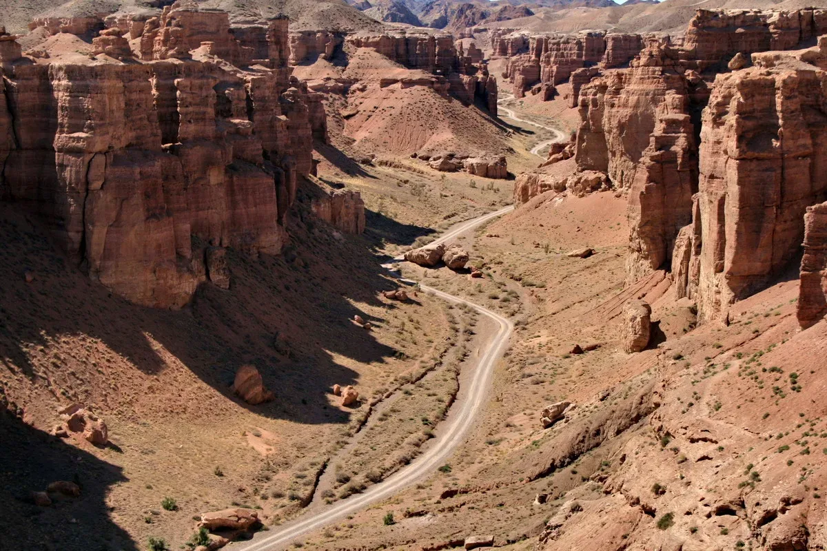 Aerial view of Charyn Canyon's Valley of Castles, with towering red-orange sandstone columns rising on both sides of a winding road on the canyon floor.