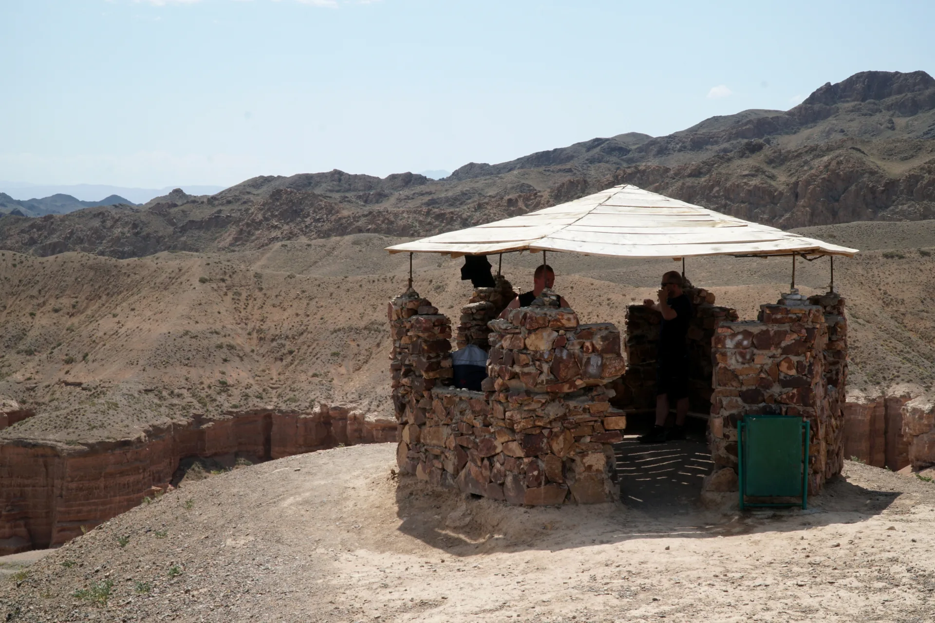 Red Charyn Canyon walls enclosing a narrow sandy floor with sparse shrubs.