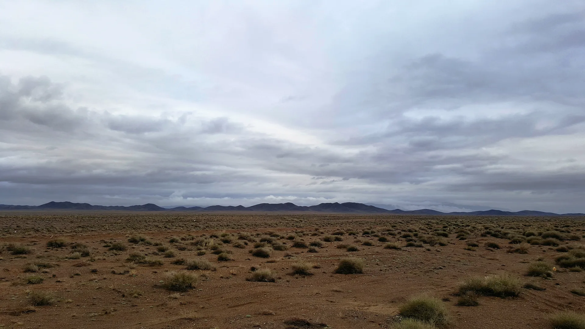 Straight highway crossing semi-desert steppe toward distant blue mountains near Chundzha.
