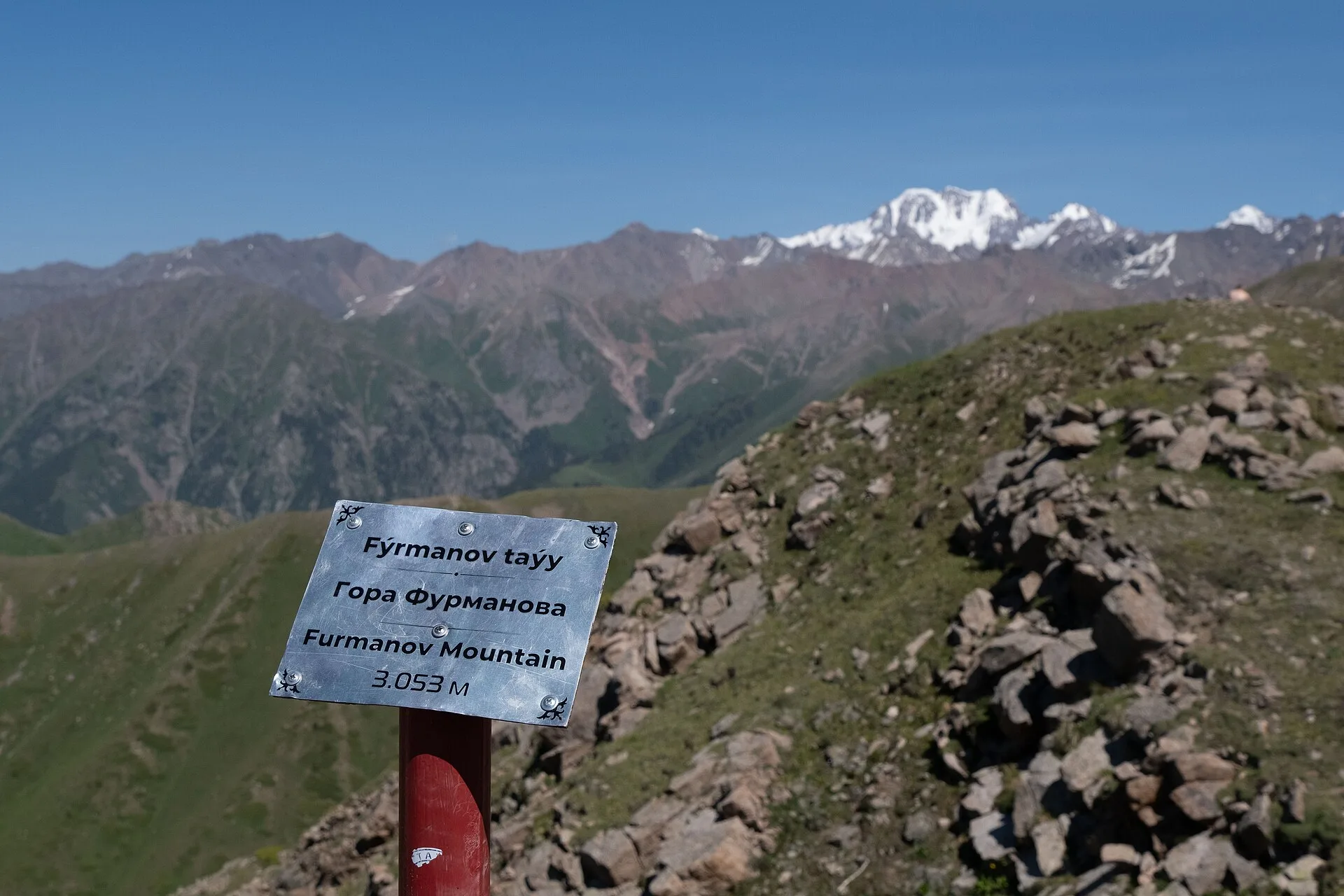 Rocky Furmanov Peak ridge with distant Talgar Peak and alpine slopes beyond.
