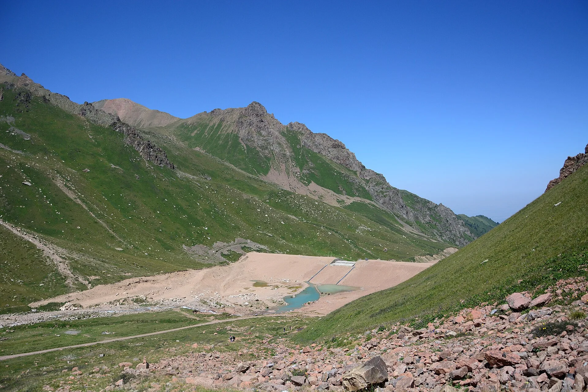 Concrete dam and rocky high-alpine basin below the Tuyuksu glacier route.