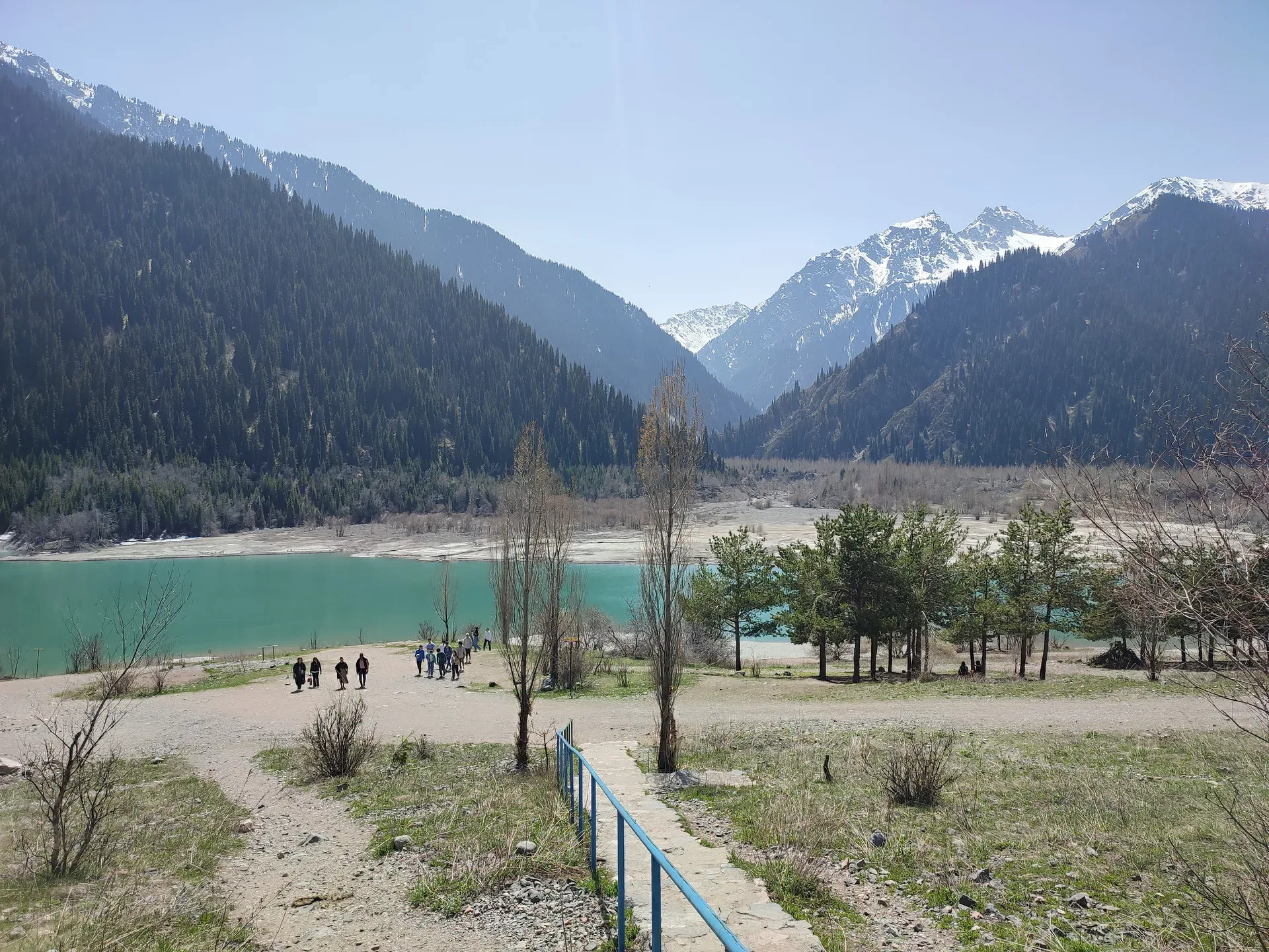 Turquoise water of Issyk Lake in the Ile-Alatau National Park gorge, with snow-capped peaks and spruce forest in spring.