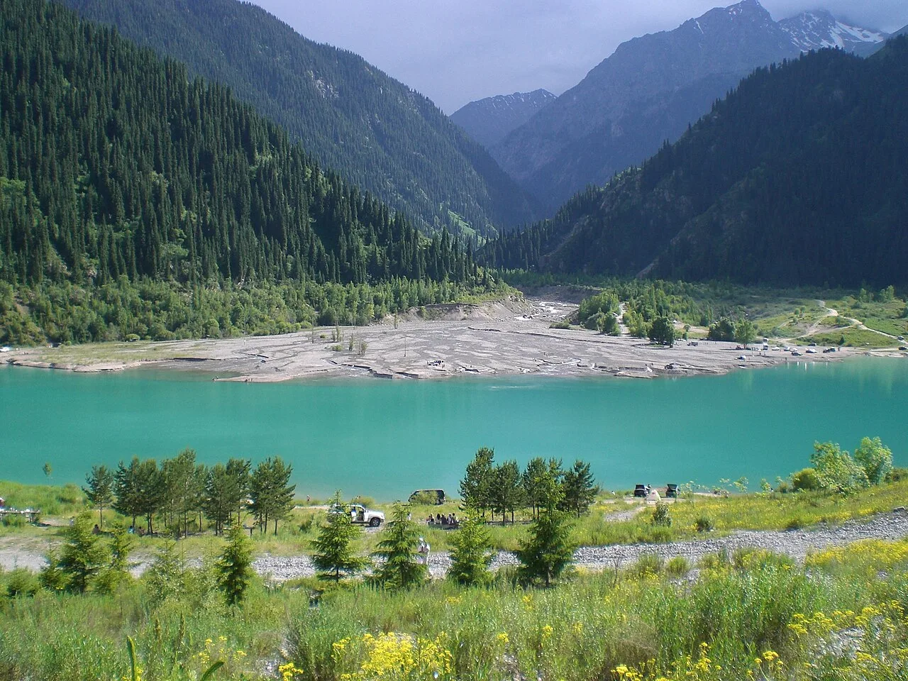 Blue-green Issyk Lake water enclosed by forested mountain slopes.