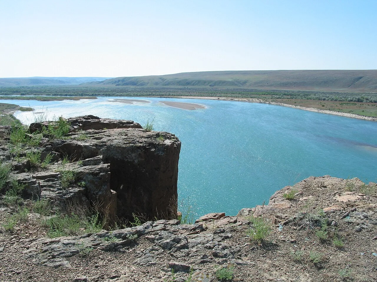 Ili River flowing between flat banks with low vegetation, representative of the Kapchagai crossing corridor.