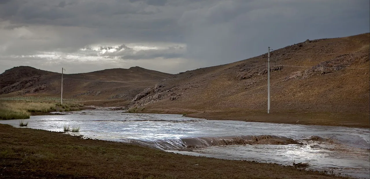 Wide Tamgaly gorge landscape with dark rock slopes and dry grass near the reserve approach road.