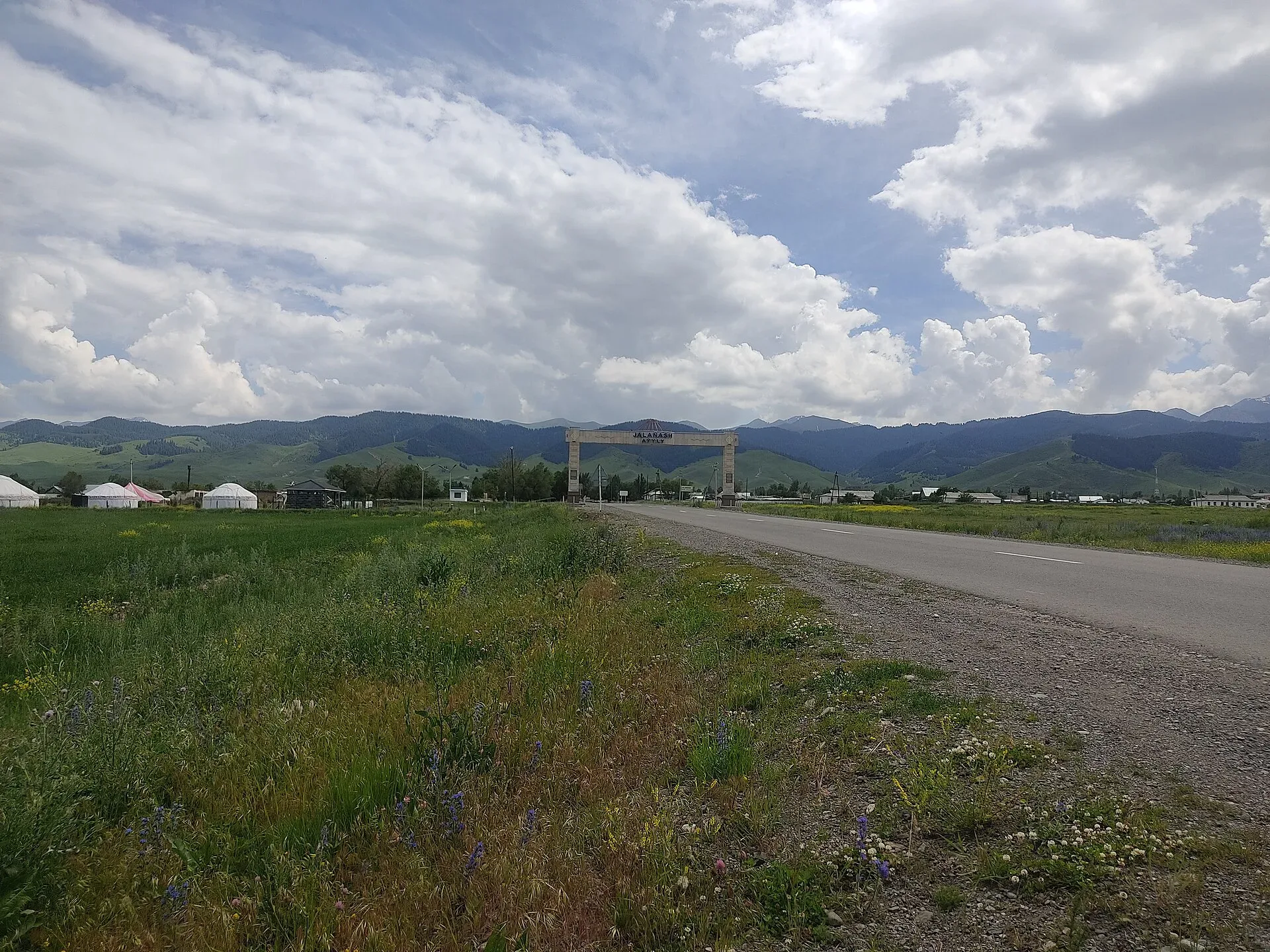 Entry road to Zhalanash village in Kegen District, Almaty Region, with flat steppe and low hills in the background