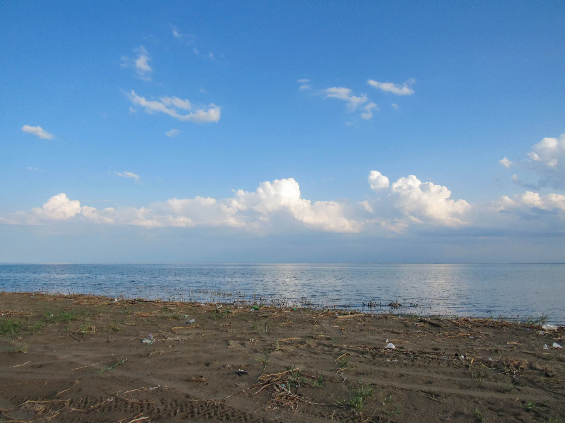 Shoreline of the Kapchagai reservoir in the Konaev district, with calm water beside a gravel bank.
