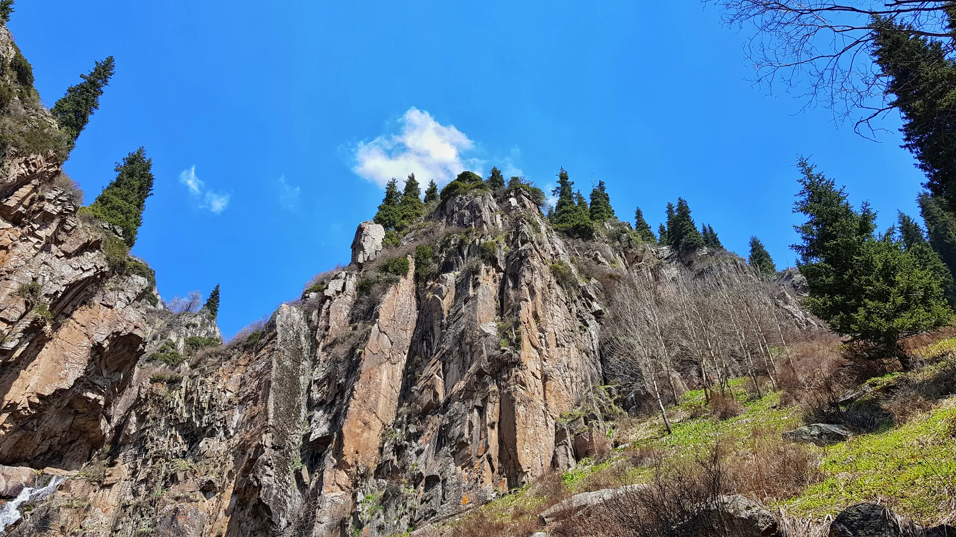 Tree-lined Butakovka gorge trail approaching the lower waterfall through the Ile-Alatau foothills.