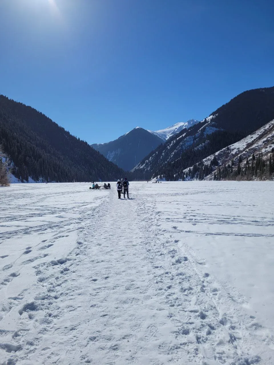 Frozen lower Kolsai Lake in winter, surrounded by snow-covered spruce trees.