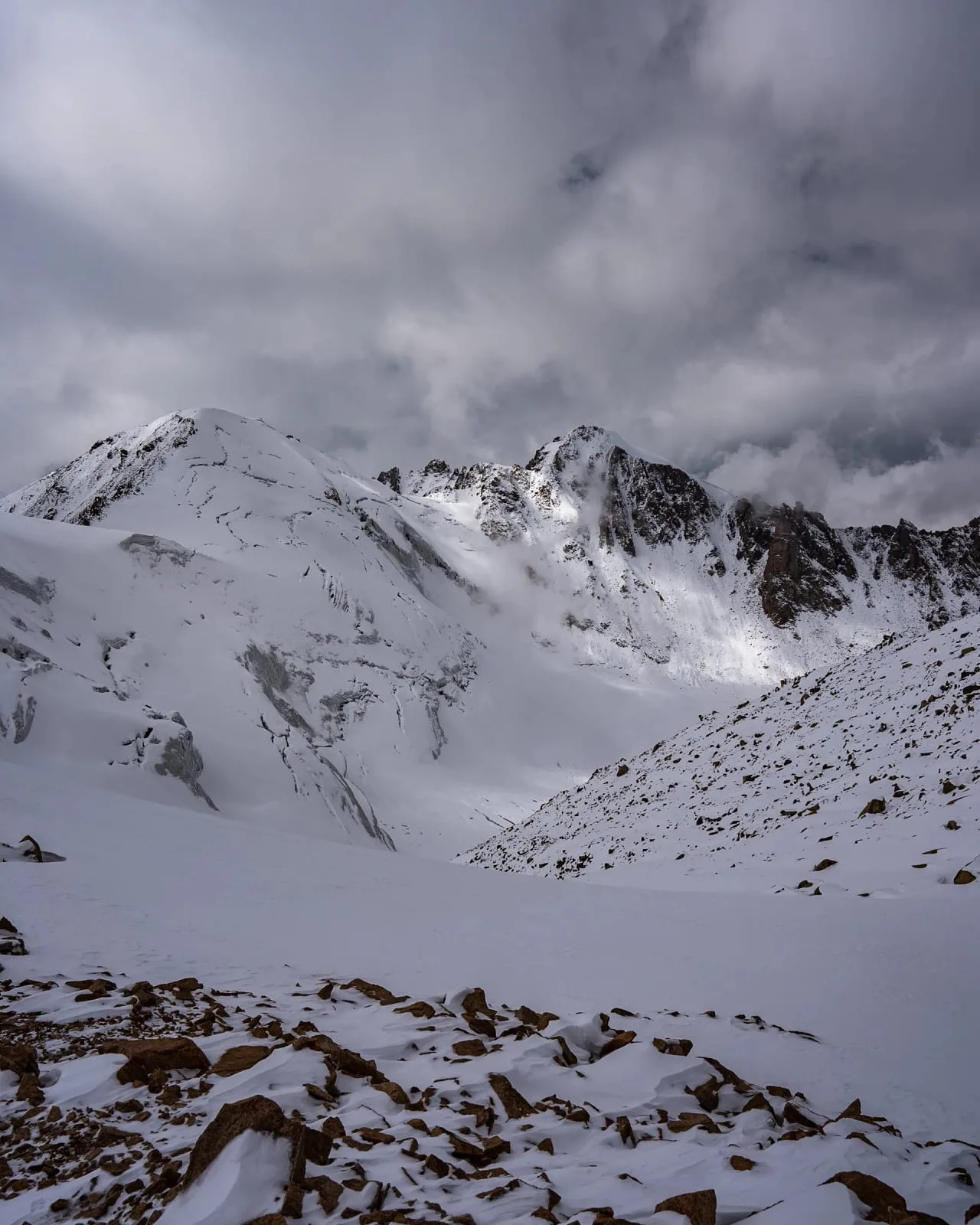 Context near Mynzhylki Plateau And Dam 3 000 M: Rocky moraine terrain above Tuyuksu Gate with glacier and snow slopes visible in the cirque.