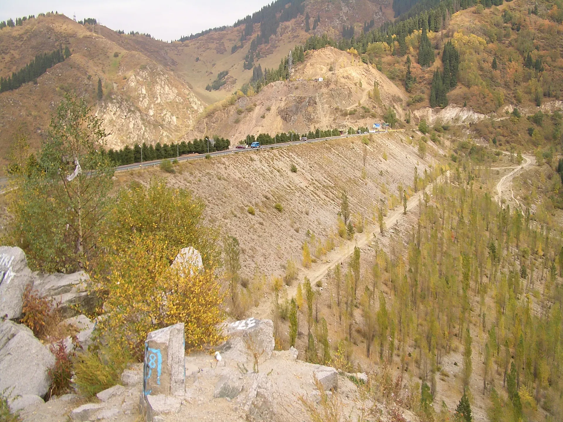 Upper Shymbulak valley with rocky gorge walls and a dirt track leading toward the higher glacier route.