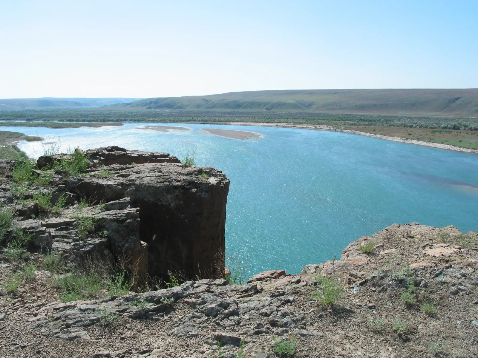 Ili River flowing through flat agricultural terrain in Almaty Oblast, Kazakhstan, low scrub vegetation on both banks under summer light