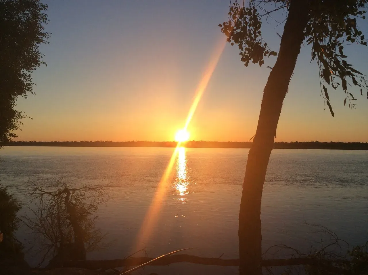 Ile River at sunset with flat sandy banks and the distant Dzungarian Alatau ridge on the horizon.
