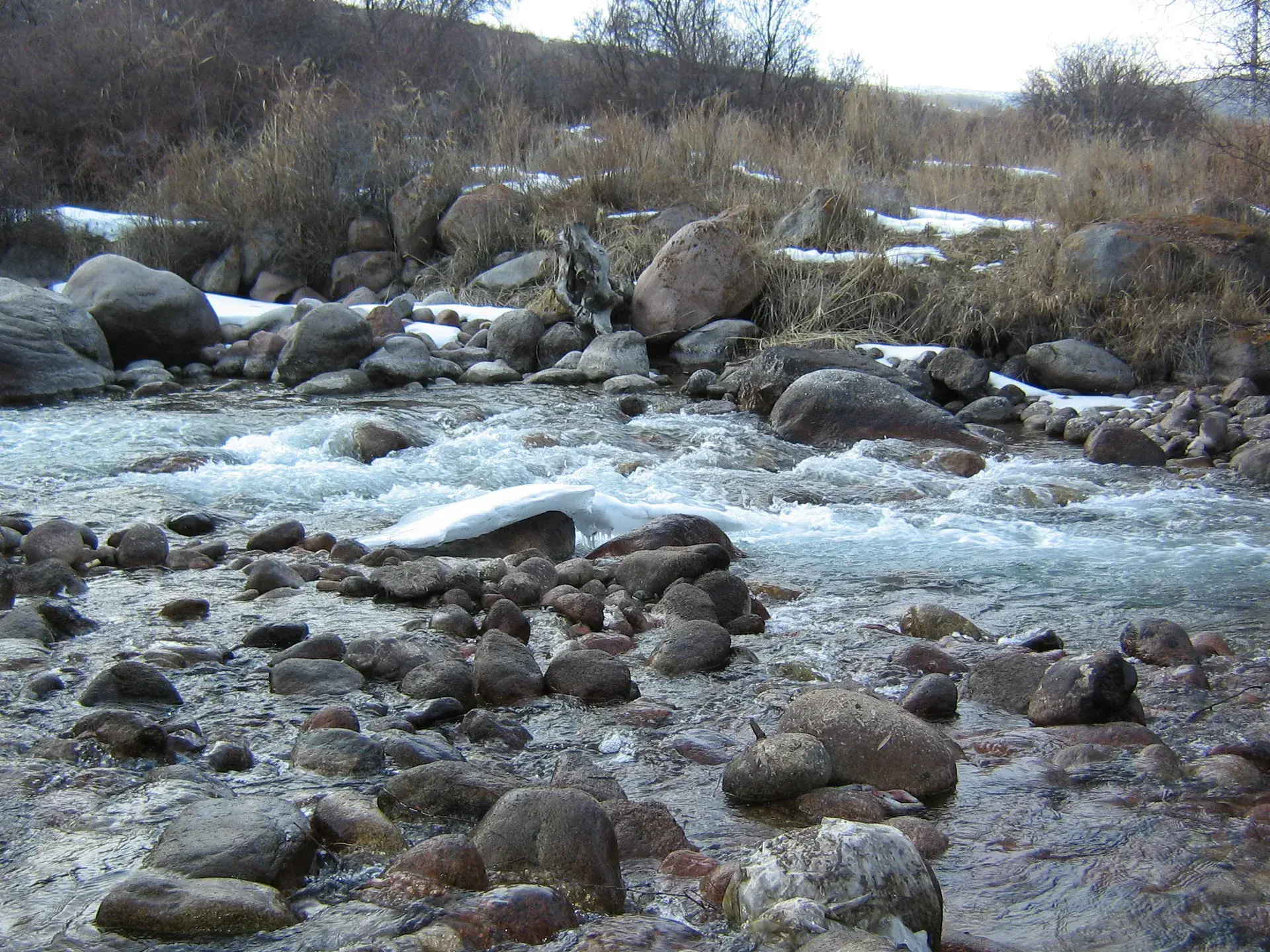 Kaskelen River running clear between rocky forested banks with snow dusting the surrounding hillsides.