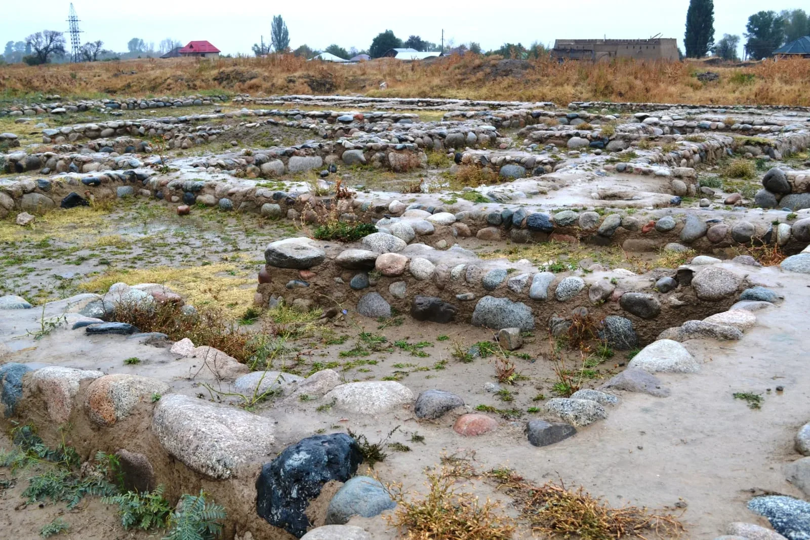Context near Talgar Town: Low earthen ramparts at the Talkhiz archaeological site with mountains beyond the open ground.