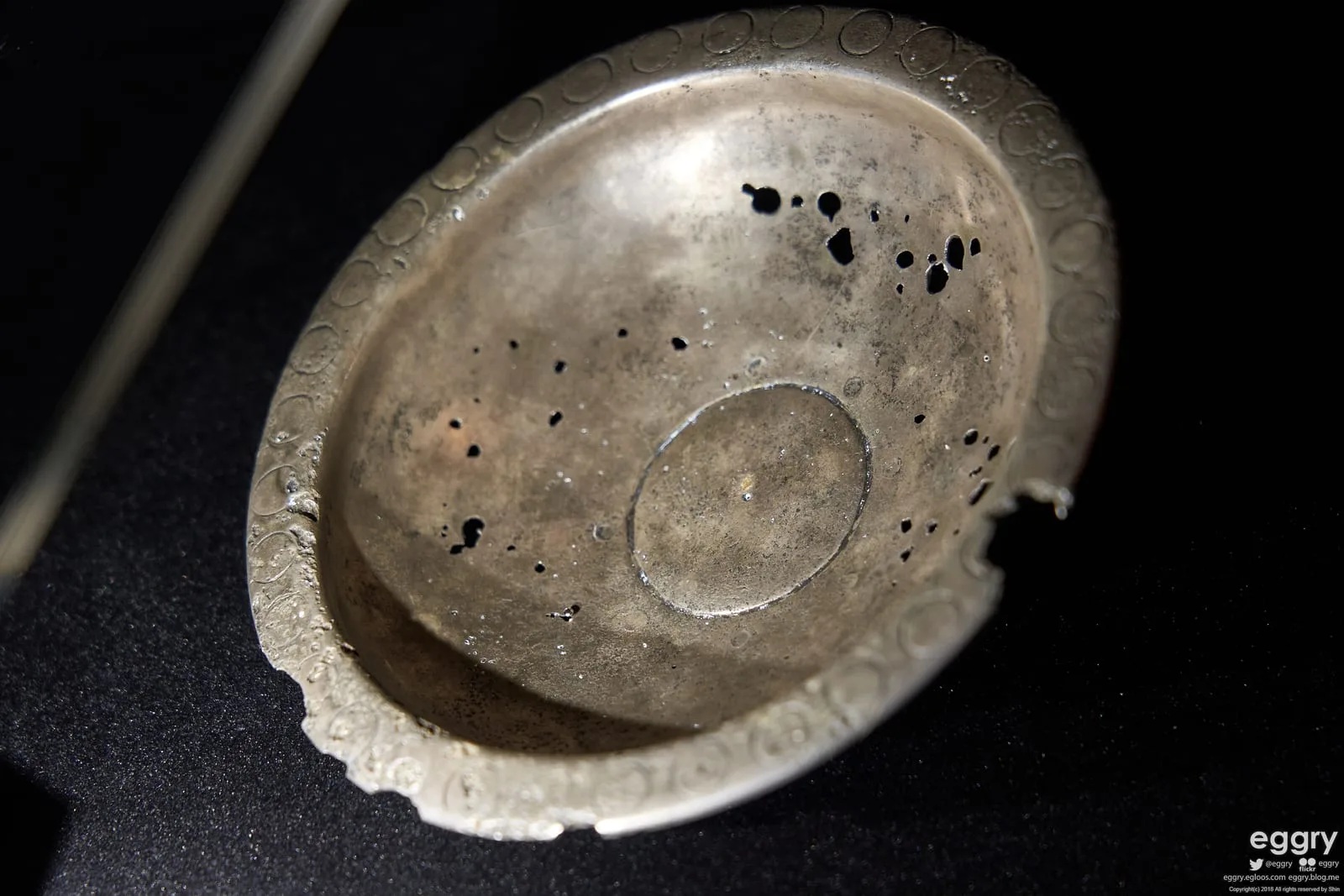 Close-up of the Issyk kurgan metal bowl with a dark museum background.