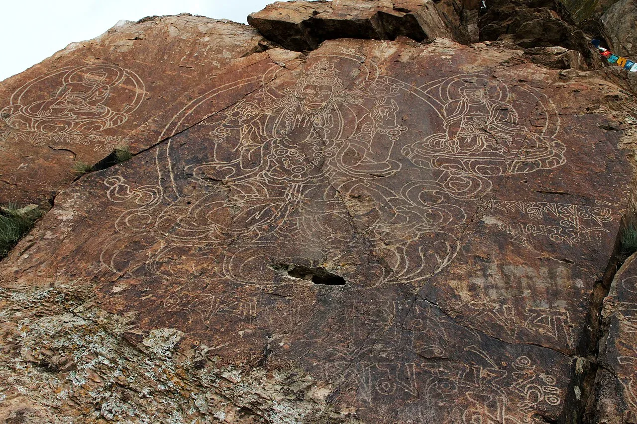 Detailed sandstone rock face at Tamgaly-Tas showing carved Buddhist figures and Tibetan script on cliffs above the Ili River.