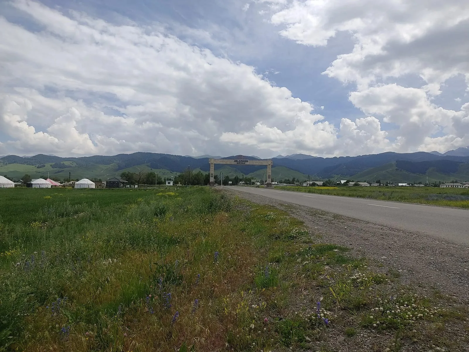 Context near Tekes Riverbank: Entry road to Zhalanash village with flat steppe and low hills in the Kegen District background.