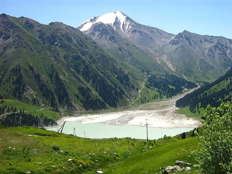 Context near Tien Shan Astronomical Observatory 2 735 M: June shoreline of Big Almaty Lake with turquoise water below bare mountain slopes.
