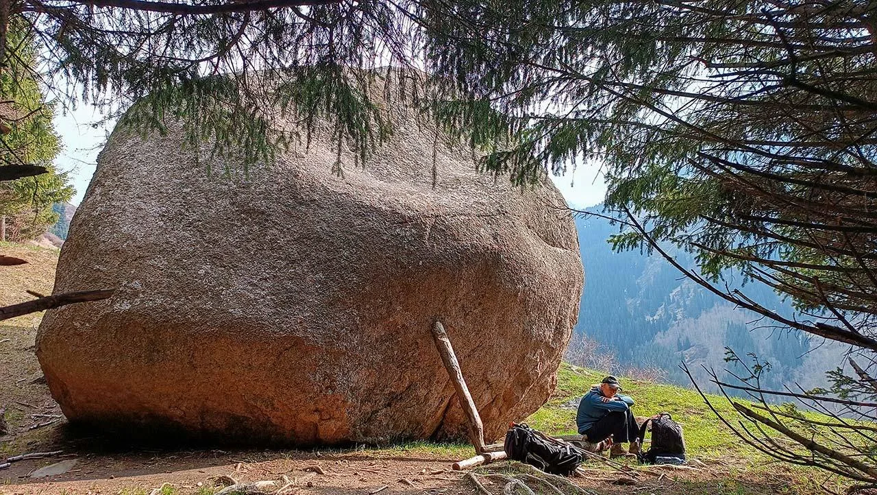 Large Uy-Tas boulder beside the Kaskelen gorge ridge trail with hikers nearby for scale.