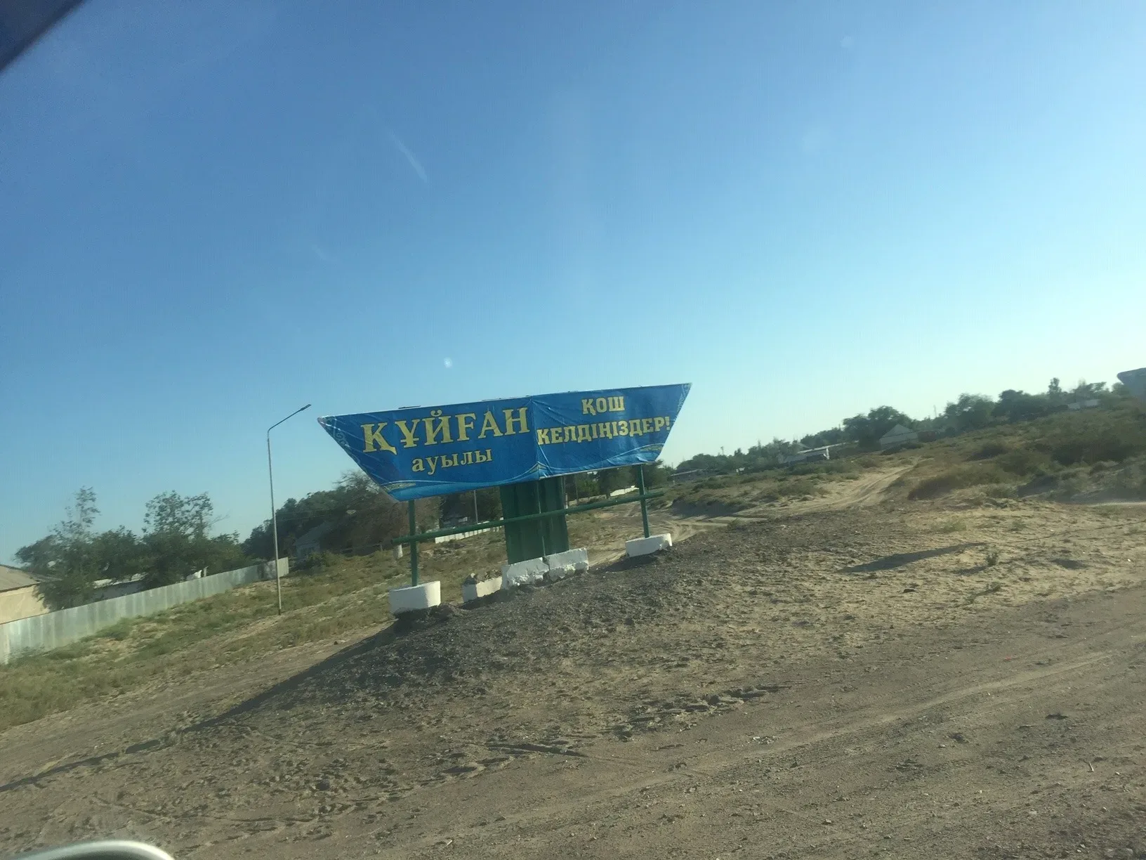 Small agricultural settlement on the Ile River bank with flat-roofed mud-brick buildings and reed-lined riverbank in the foreground