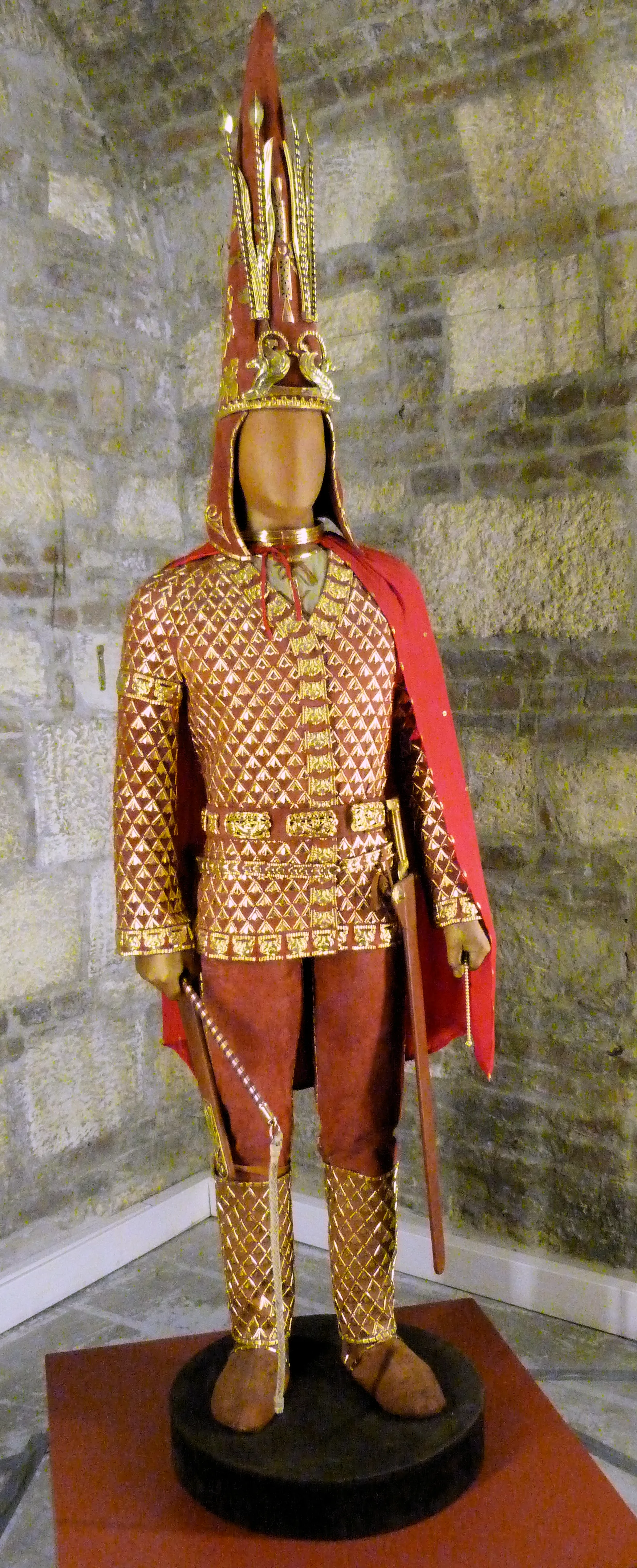 Full reconstructed Saka Golden Warrior figure from the Issyk kurgan in gold-plated scale armour and tall conical headdress, displayed against a plain background