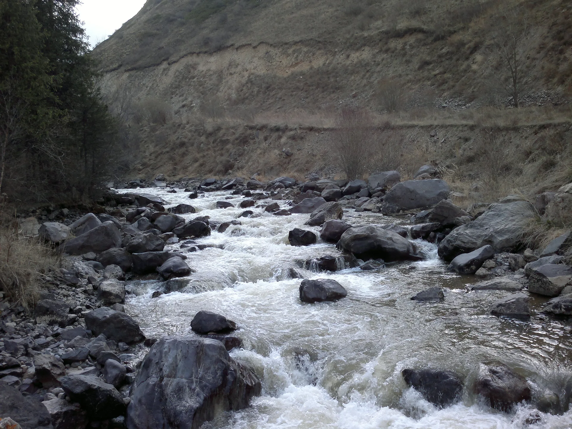Turgen River valley road winding through the Enbekshikazakh District of Almaty Region, Kazakhstan, with green hills on either side.