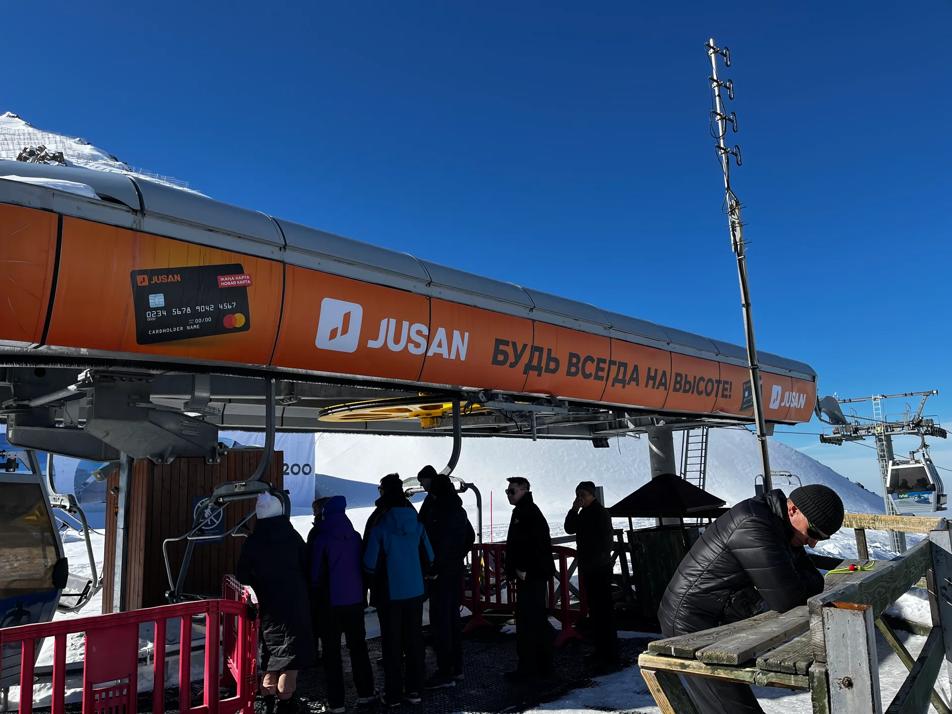 Shymbulak cable car upper station in winter at approximately 3,200 m, with gondola terminal buildings and snow-covered ridge behind
