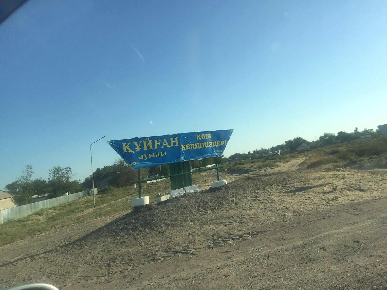 Small agricultural settlement on the Ile River bank with flat-roofed mud-brick buildings and reed-lined riverbank in the foreground